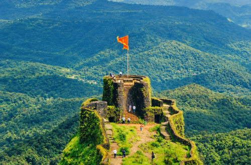 Raigad Fort surrounded by lush green Sahyadri mountains with a saffron flag