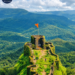 Raigad Fort surrounded by lush green Sahyadri mountains with a saffron flag