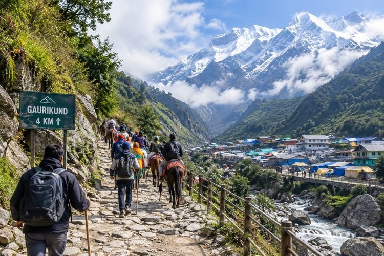 Pilgrims trekking along the Kedarnath trail near Gaurikund with snow-covered Himalayan mountains