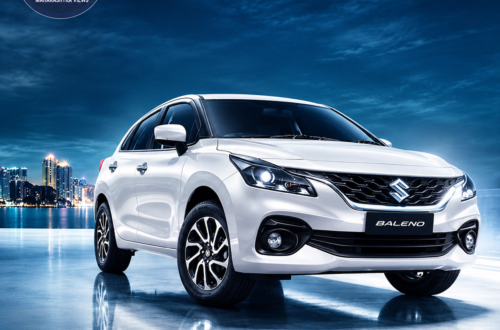White Maruti Suzuki Baleno on a wet reflective surface at night, with a city skyline in the background and the Maharashtra Views logo in the upper-left corner.